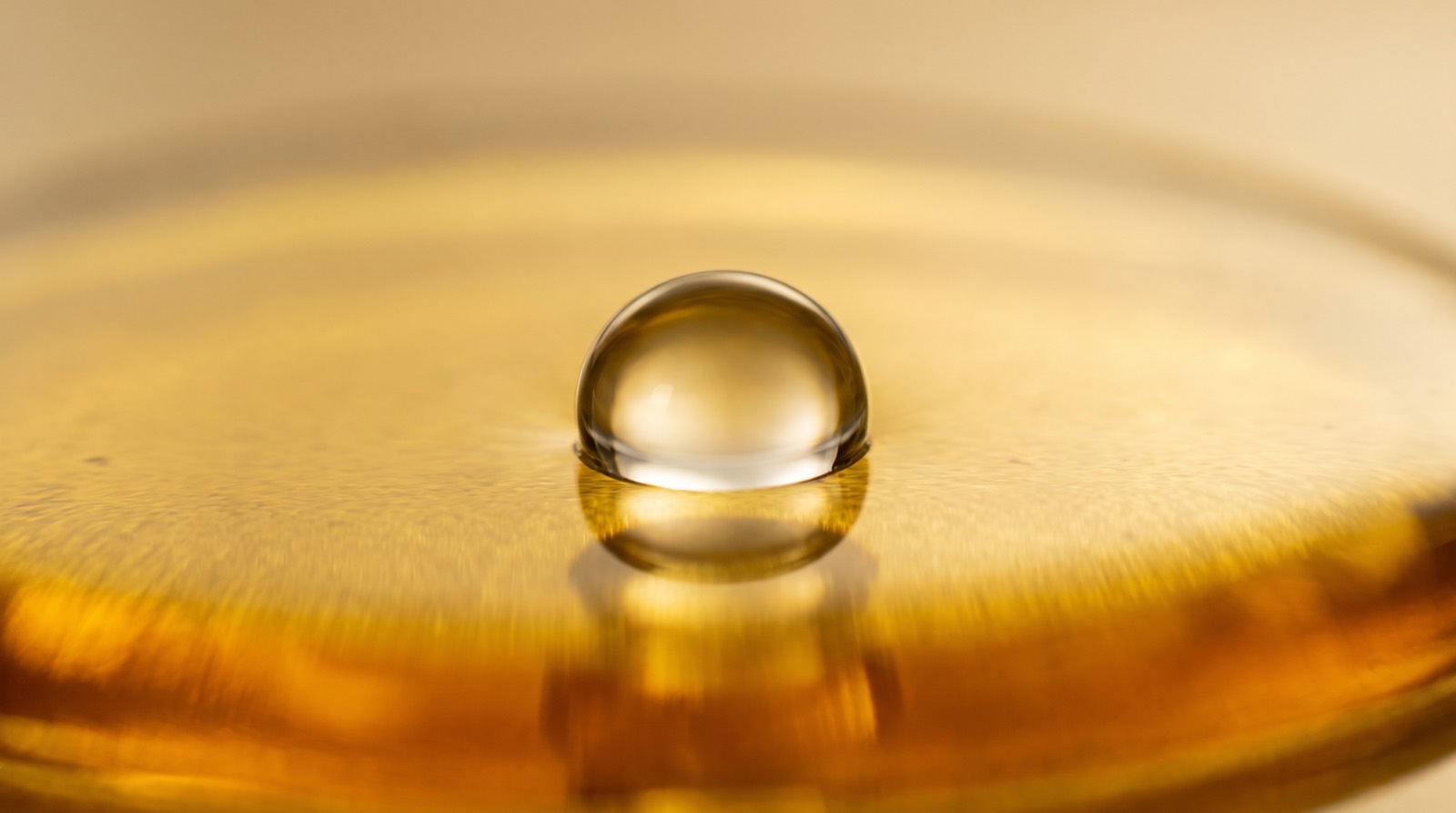 Makroaufnahme eines klaren Wassertropfens, der auf einer goldenen Öloberfläche perlt