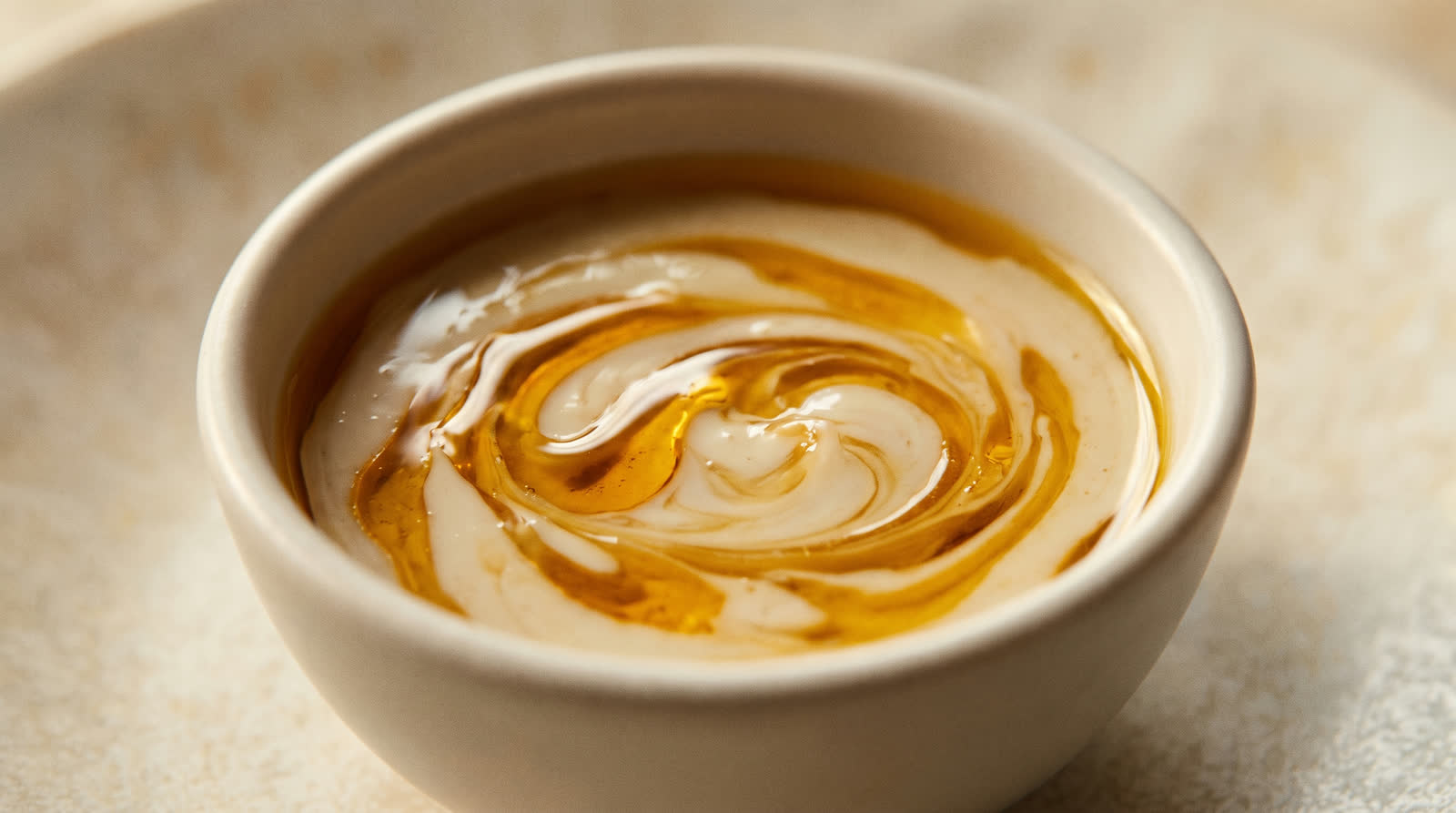 Makroaufnahme eines goldenen Öl-Serums, das sich in eine helle Creme legt