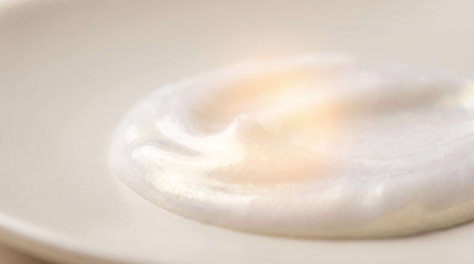 Makroaufnahme einer perlmuttweißen Sonnencreme-Textur mit sanftem Lichtreflex
