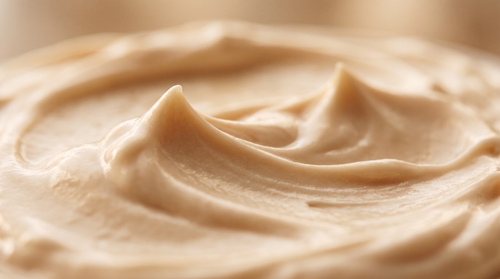 Makroaufnahme einer dicken, satten Cremeschicht mit weichen Spuren auf warmem Beige